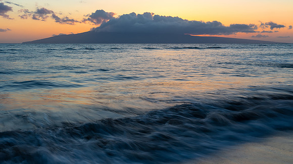 Orange sun light at sunset reflected off the gentle Maui surf.