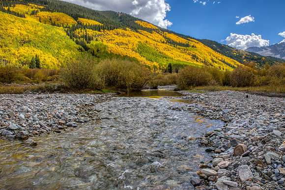16.4 MB, 5184 x 3456: A mountain stream flows past a hillside of autumn colored yellow and green aspen trees.