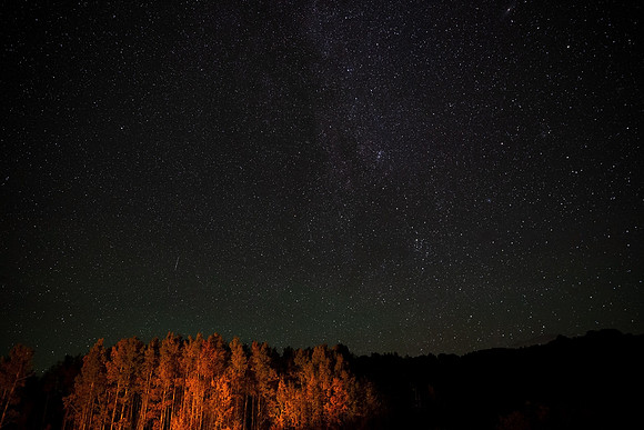 11.1 MB, 5184 x 3456: Stars and the milky way on a clear Colorado night while pine trees glow from a camp fire nearby.