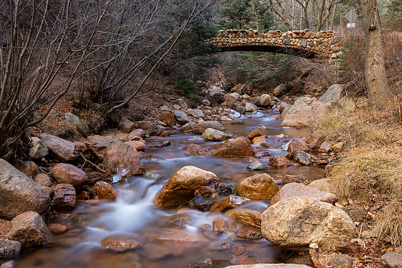 20.6 MB, 5184 x 3456: Stream flows under an old stone bridge and over large rocks.