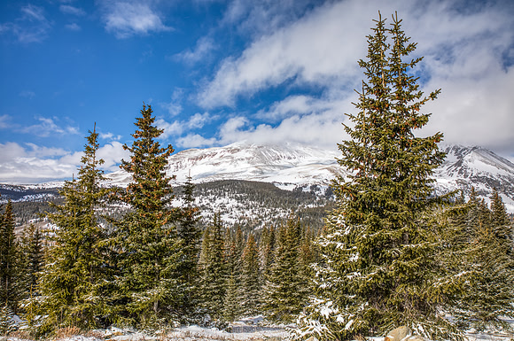 30.6 MB, 6704 x 4456: Snow covered mountain peaks and green pine trees under partly cloudy skies
